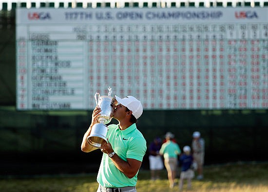 With red numbers on the scoreboard in the background, Brooks Koepka kisses the trophy Sunday after winning the U.S. Open at Erin Hills in Erin, Wis.