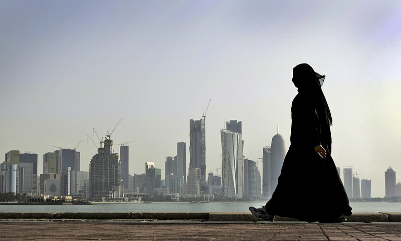 FILE- In this May 14, 2010 file photo, a Qatari woman walks in front of the city skyline in Doha, Qatar. An investigation into why a British man fell to his death on a Qatar World Cup site has raised concerns about stadium roof safety. Acting as a mediator, Kuwait has presented Qatar a long-awaited list of demands from Saudi Arabia, Bahrain, the United Arab Emirates and Egypt, four Arab nations that cut ties with Qatar in early June, 2017. (AP Photo/Kamran Jebreili, File)