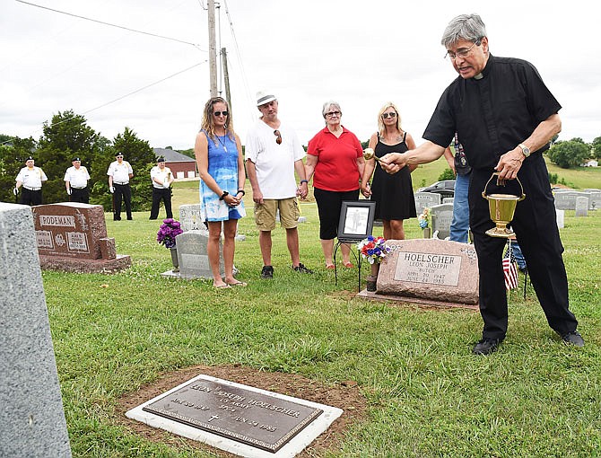 Fr. Ignazio Medina, at right, says a prayer as he sprinkles holy water on the newly installed footstone for Army veteran Leon Hoelscher. Hoelscher's widow, Elizabeth Hoelscher-Siebeneck, third from left, has worked for years to get him the brass marker at his grave, and Thursday, it finally happened. Standing with Hoelscher-Siebeneck are her children, from left, Sarah Struemph, Mike Hoelscher and Rebecca Hoelscher.