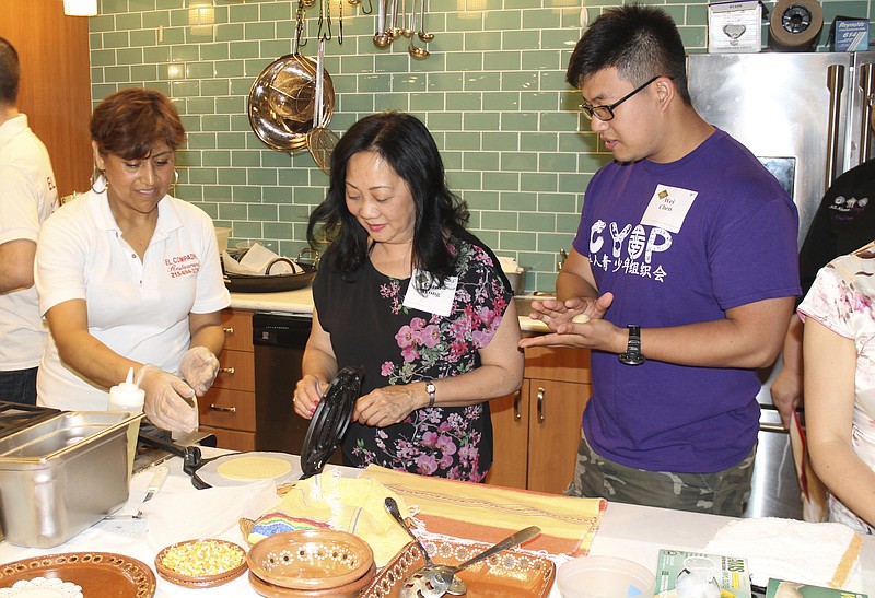 In this photo provided by Alex Styer, Cristina Martinez, left, co-owner of the Mexican restaurant El Compadre in Philadelphia, teaches Carol Wong, center, and Wei Chen, right, how to press tortillas during a June 5, 2017, dinner at Reading Terminal Market in Philadelphia. People of different backgrounds are sharing meals from their cultures as part of a yearlong program titled "Breaking Bread, Breaking Barriers," which organizers say uses good food to help connect groups that might have divisions. (Alex Styer/Bellevue Communications Group via AP)