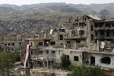 In this May 18, 2017 file photo, a Syrian National flag hangs out of a damaged building at the mountain resort town of Zabadani in the Damascus countryside, Syria. The Syrian government on Tuesday, June 27, 2017 dismissed White House allegations that it was preparing a new chemical weapons attack, as activists reported an airstrike on an Islamic State-run jail in eastern Syria that they said killed more than 40 prisoners.