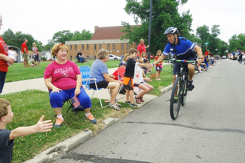 <p>Helen Wilbers/FULTON SUN</p><p>Fulton police officer Adam Cramer hands out high-fives along the Fulton Independence Day Parade route. Eli Lickey (orange shorts) said the police were his favorite part of the parade.</p>