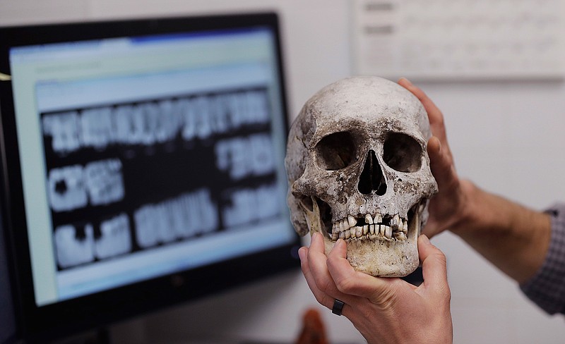 In this Wednesday, April 12, 2017, photo, Dr. Tim Gocha uses dental records as he works to help identify the remains of immigrant who died along the U.S-Mexico border, at the Forensic Anthropology Center at Texas State, in San Marcos, Texas. Forensic investigators and advocacy groups said efforts to identify the remains of immigrants found along the Texas-Mexico border remain slow because DNA comparisons aren't being made with a large pool of potential family members. DNA extracted from immigrants' remains in Texas ends up in an FBI database.