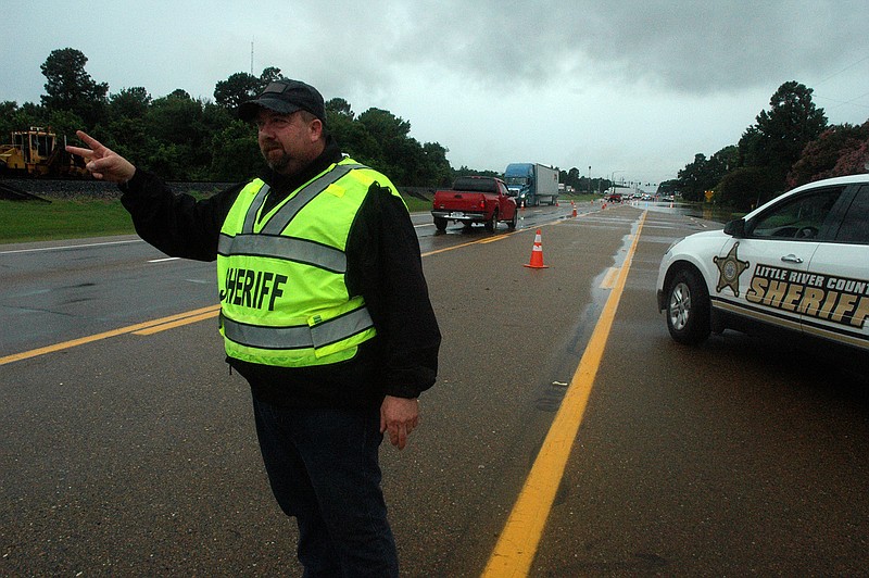 Little River County Sheriff's Deputy Tim Garner motions to northbound traffic to slow down as they approach floodwater Wednesday morning on U.S. Highway 71. The floodwaters were receding by about 1 p.m.