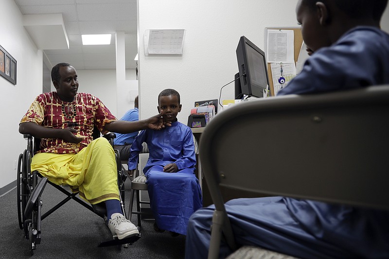 Ali Said, of Somalia, left, waits at a center for refugees with his two sons Thursday, July 6, 2017, in San Diego. Said, whose leg was blown off by a grenade, says he feels unbelievably lucky to be among the last refugees allowed into the United States before stricter rules kick in as part of the Trump administration's travel ban. (AP Photo/Gregory Bull)
