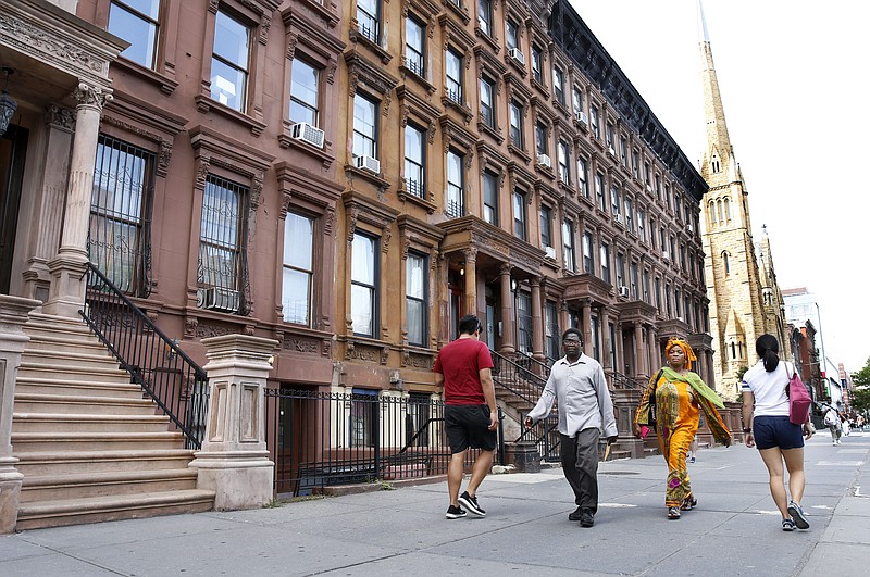 People stroll down the sidewalk along Malcolm X Boulevard, Monday, June 26, 2017, in New York, where residents are upset about a realtor's proposed neighborhood name change from southern Harlem to SoHa. Many residents say the name change devalues the area's rich political and cultural history. (AP Photo/Kathy Willens)