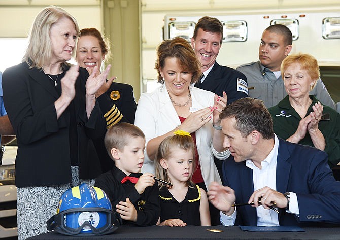 Rep. Jeanie Lauer, standing at left, and Darlene Shelton, center of middle row, applaud as Gov. Eric Greitens hands a pen to Danny Shelton, 6, and his sister, Lilyan, 5, after using them to sign Senate Bill 503 into law Tuesday morning at Jefferson City Fire Station No. 3. The new law gives first responders more access to resources as well as allows regional medical directors to provide medical direction by telecommunication.