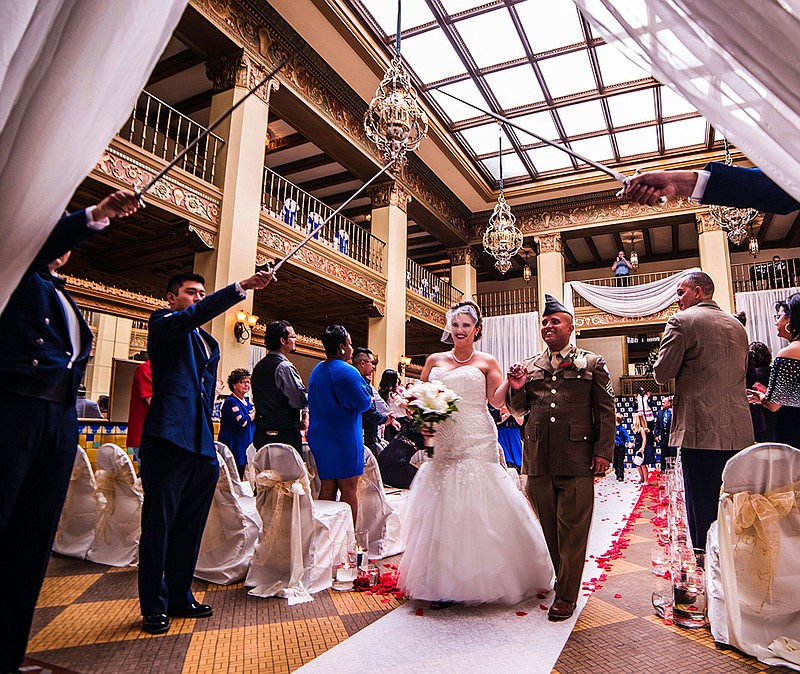 In this July 8, 2017 photo, Mr. and Mrs. Jeffrey Mercado exit the Grand Lobby of the Cactus Hotel underneath a traditional military cordon steel arch in San Angelo, Texas. White linens, blue flowers and period piano music from the 1940s filled the Cactus Hotel on Saturday for a donated wedding to remember. 