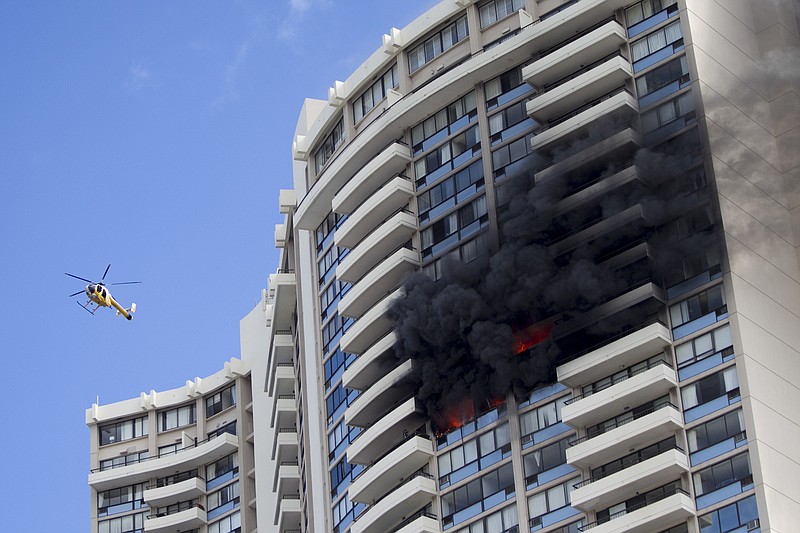 A Honolulu Fire Department helicopter flies near a fire burning on a floor at the Marco Polo apartment complex, Friday, July 14, 2017, in Honolulu. (AP Photo/Marco Garcia)