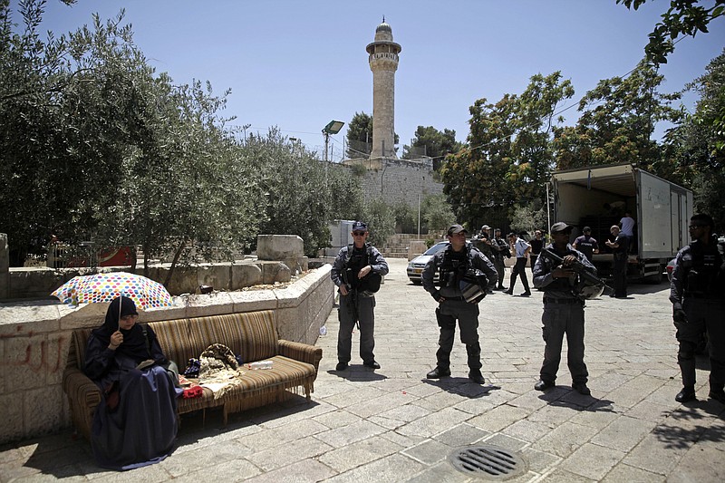 Israeli border police officers stand guard as a Palestinian woman sits outside the Al Aqsa Mosque compound, in Jerusalem, Sunday, July 16, 2017. Adnan Husseini, the Palestinian Minister of Jerusalem, said Sunday that arrangements at the Muslim-administered holy site need to return to how they were before a deadly attack last week, in which three Arab Israelis shot dead two police officers before being killed. (AP Photo/Mahmoud Illean)