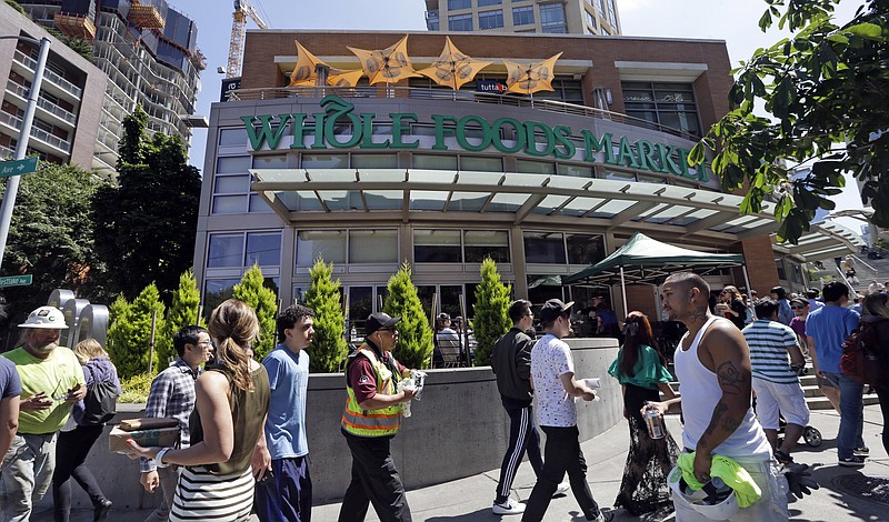 In this Tuesday, July 11, 2017, photo, pedestrians walk past a Whole Foods Market, just down the street from the headquarters of Amazon, in Seattle. Amazon, already a powerhouse in books, shoes, streaming video, electronics and just about everything else, will bind its customers even more closely once it completes its $13.7 billion bid for the organic grocer Whole Foods. Although antitrust lawyers believe the deal will get approved, many customers and experts alike worry about two big companies combining into a bigger one. (AP Photo/Elaine Thompson)