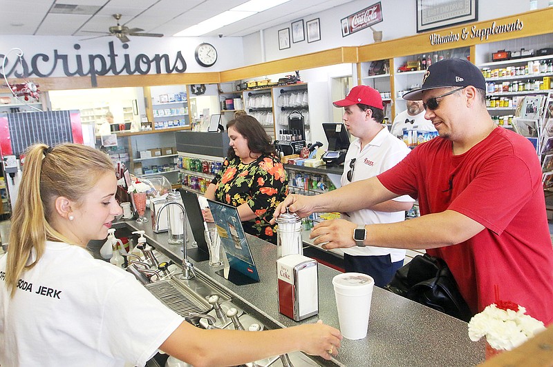Bailey Conrad, 18, left, makes ice cream floats and fountain sodas Tuesday for customers, including Chris Scheppers, right, at Whaley's East End Pharmacy. The pharmacy recently brought ice cream back to its soda fountain.