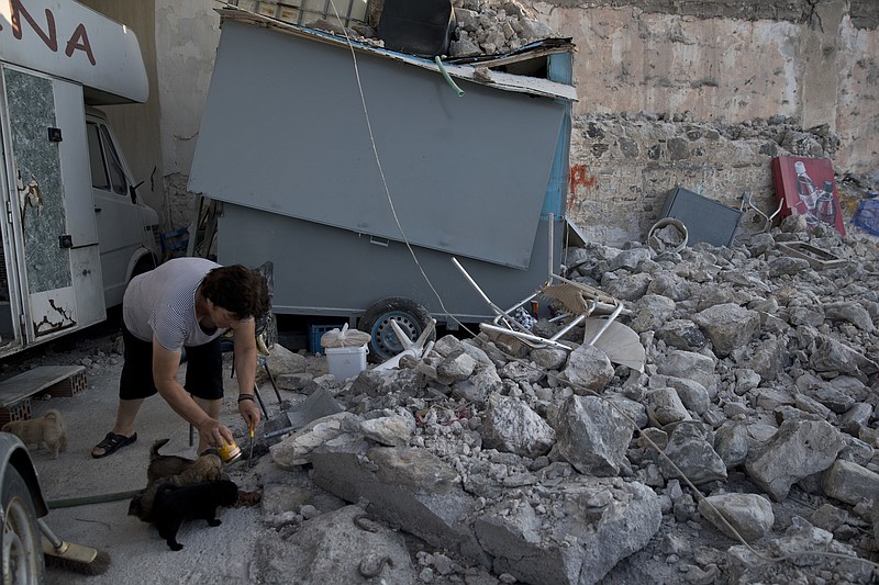 A woman feeds puppies next to rubble, following an earthquake at the port of Kos island, Greece, on Saturday, July 22, 2017. Hundreds of people on the eastern Greek island of Kos have spent the night sleeping outdoors after a powerful Friday earthquake killed two tourists and injured nearly 500 others across the Aegean Sea region in Greece and Turkey.(AP Photo/Petros Giannakouris)