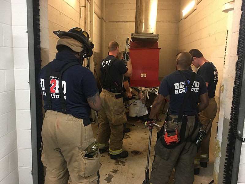 In this photo provided by DC Fire and EMS, emergency personnel respond to a call from a man who was stuck in a trash chute, early Sunday, July 23, 2017, in Washington. Spokesman Vito Maggiolo says the man was throwing out trash at the apartment building when he thought he dropped a cellphone in the chute. Maggiolo says the man leaned in to check and fell inside.