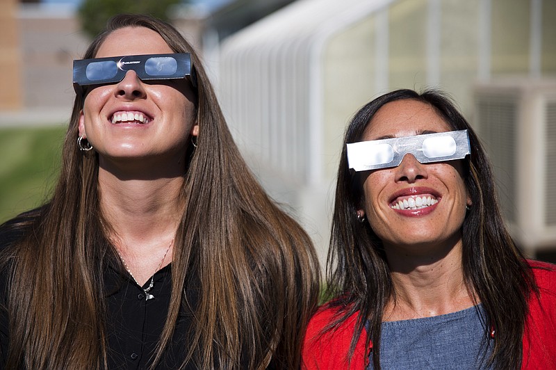In this Tuesday, July 18, 2017 photo, Twin Falls High School science teachers Ashley Moretti, left, and Candace Wright, right, use their eclipse shades to look at the sun as they pose for a portrait at Twin Falls High School in Twin Falls, Idaho. The district bought 11,000 pairs of solar glasses, enough for every student and staff member to view the solar eclipse Aug. 21, from Twin Falls.  (Pat Sutphin/The Times-News via AP)