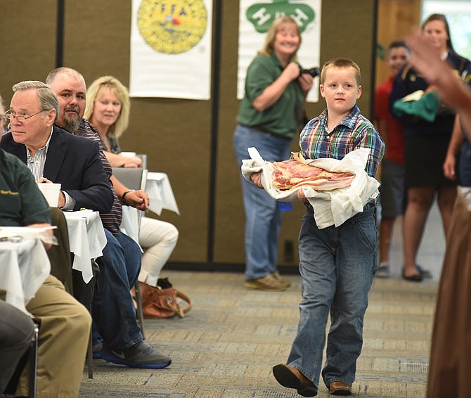 Oliver Sullivan looks to the auctioneer as he carries his bacon slab in front of the bidding crowd during Friday's Cole County Fair Ham and Bacon Breakfast and Auction at the Missouri Farm Bureau headquarters.