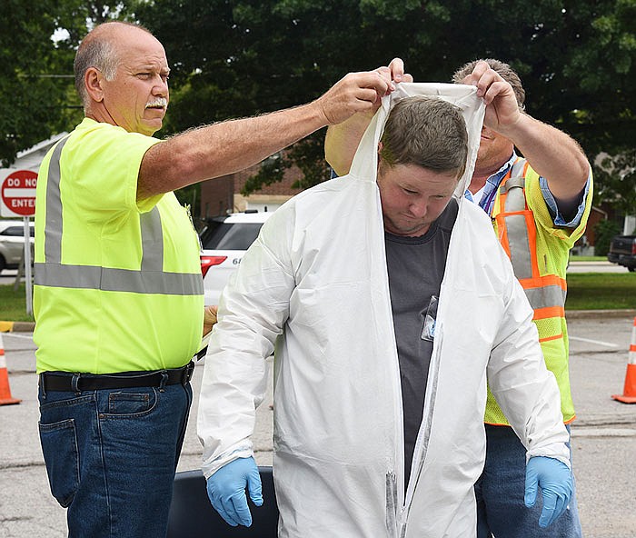 After being inspected for radiation exposure, Mike Belt, left, and Scott Campbell remove the hazardous material suit worn by Wesley Prenger. They followed step-by-step instructions for removal, which includes rolling the suit into itself as it's removed.