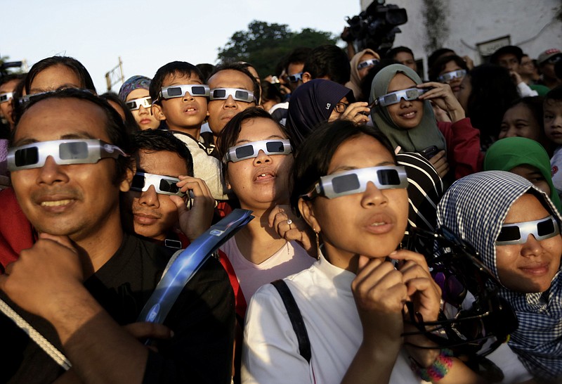 FILE - In this Wednesday, March 9, 2016 file photo, people wearing protective glasses look up at the sun to watch a solar eclipse in Jakarta, Indonesia. Doctors say not to look at the sun without eclipse glasses or other certified filters except during the two minutes or so when the moon completely blots out the sun, called totality. That’s the only time it’s safe to view the eclipse without protection. When totality is ending, then it’s time to put them back on.  (AP Photo/Dita Alangkara)