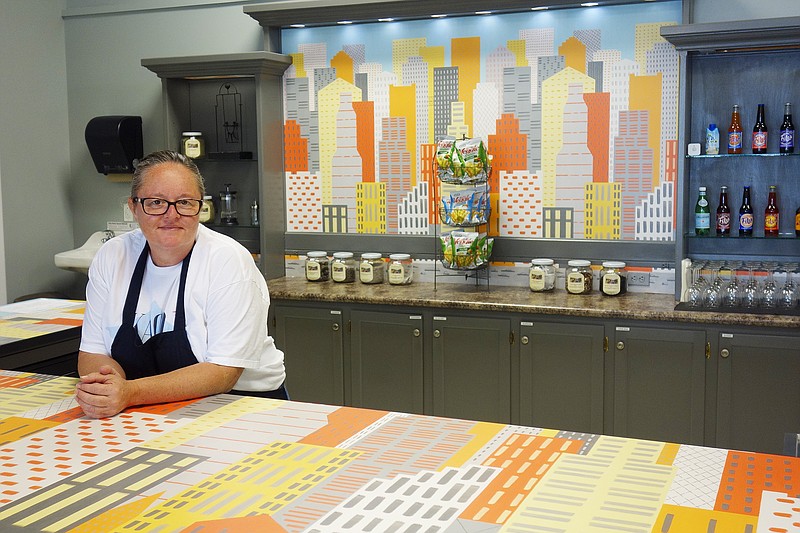Cindy Baker of KACO The Kitchen leans on her counter, decorated with cheerful WilsonArt laminant, as is the back wall. The eatery, at 600 Commons Drive in Fulton, is bright and cheerful with eat-in, carry-out, catering, delivery and more.