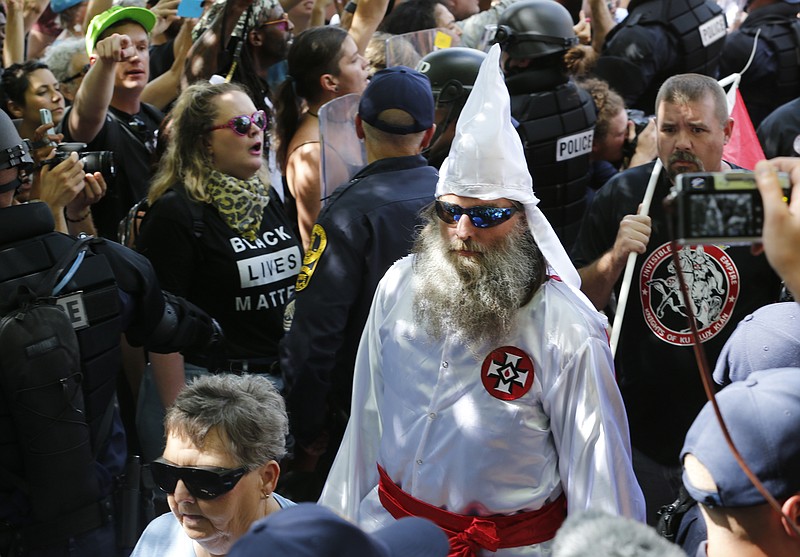 This July 8, 2017 photo shows members of the KKK escorted by police past a large group of protesters during a KKK rally in Charlottesville, Va.  Some white Southerners are again advocating for what the Confederacy tried and failed to do in the 1860s: secession from the Union. So-called Southern nationalists are within the group of demonstrators who are fighting the removal of Confederate monuments around the South. They say it’s time for Southern states to secede again and become independent of the United States..(AP Photo/Steve Helber)