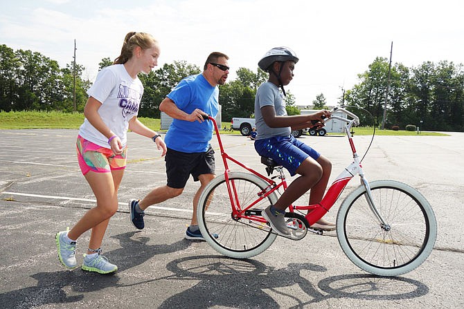  Kwadwo Wiredu, 10, gets encouragement Thursday from volunteers Bill Nigus and Channing Totta at the iCan Bike Camp in Fulton. By the end of the day, he was pedalling under his own steam for short stretches.
