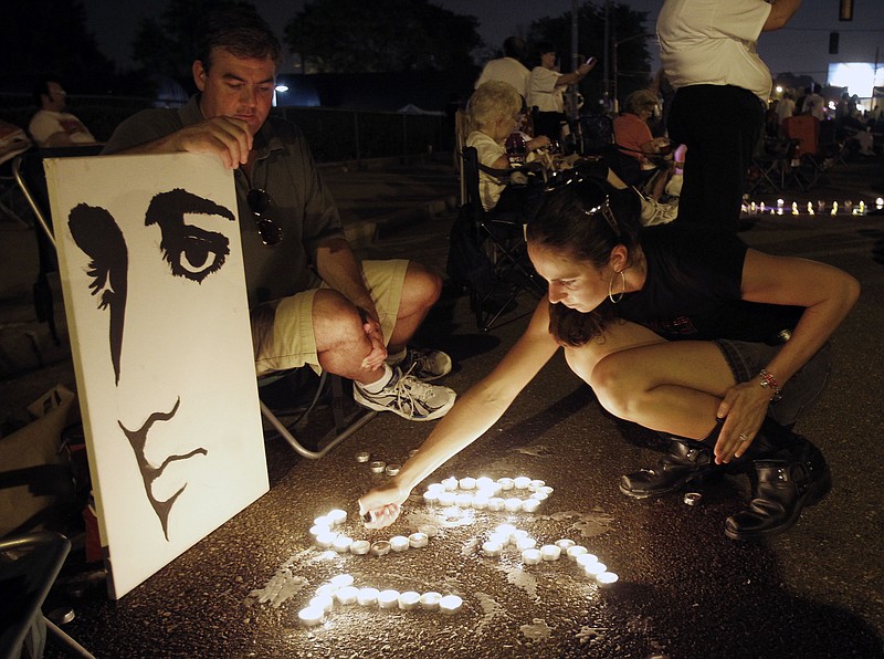 FILE- This Aug. 15, 2010 file photo shows Melanie Curry as she lights candles at an Elvis Presley display she made with Judd Cannon, left, on Elvis Presley Boulevard in front of Graceland, Presley's Memphis, Tenn. home. Friends and fans of late singer and actor Elvis Presley are descending on Memphis, Tennessee, for Elvis Week, the annual celebration of his life and career. It coincides with the 40th anniversary of the passing of Presley, who died on Aug. 16, 1977. (AP Photo/Mark Humphrey, File)