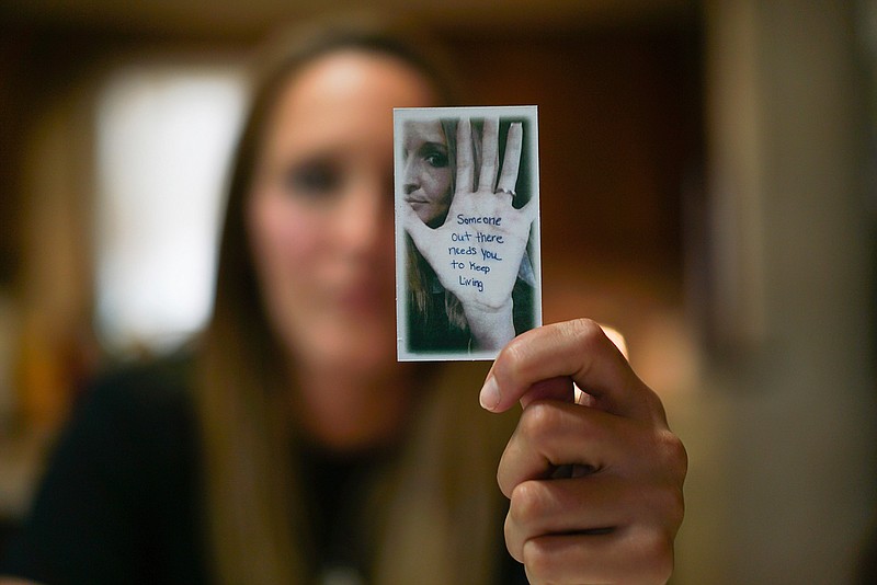 In this Aug. 9, 2017, photo, Koriann Evans, a former drug addict, holds up a photo of herself with an anti-addiction message written on her hand at her home in Bellevue, Ohio. Evans was hooked on heroin for over a decade until she overdosed while driving her car with her two children in the back, after which she stopped using drugs and started speaking about her former addiction. Police and rescue crews say drivers overdosing on heroin and other drugs are driving up the number of car crashes. 