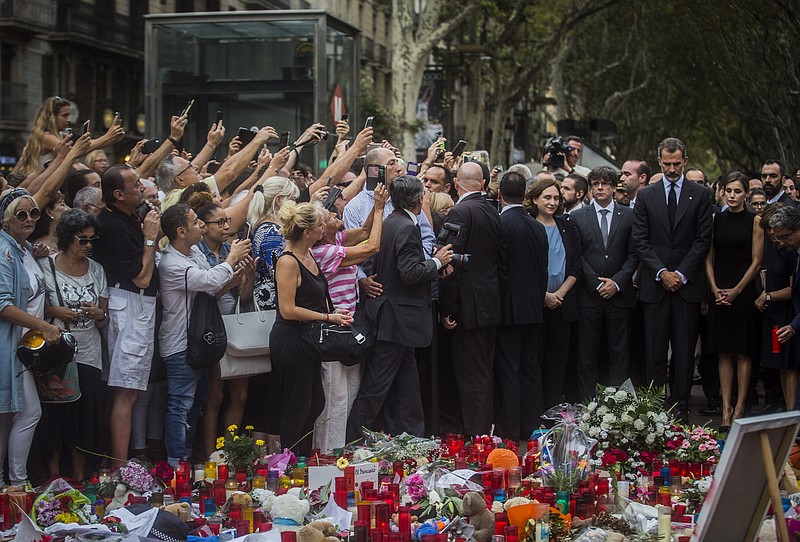 People take photos as Spain's King Felipe and Queen Letizia, right, paying respect at a memorial tribute of flowers, messages and candles to the van attack victims in Las Ramblas promenade, Barcelona, Spain, Saturday, Aug. 19, 2017. Authorities in Spain and France pressed the search Saturday for the supposed ringleader of an Islamic extremist cell that carried out vehicle attacks in Barcelona and a seaside resort, as the investigation focused on links among the Moroccan members and the house where they plotted the carnage.(AP Photo/Santi Palacios)