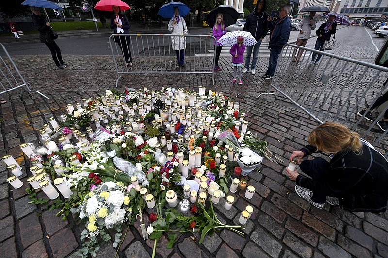 A woman places a candle by floral tributes for the victims of an attack at Turku Market Square on Friday, in Turku, Finland, Saturday, Aug. 19, 2017.  A suspect detained for allegedly stabbing two people to death in a wild knife attack in the western Finnish city of Turku is being investigated for murder with possible terrorist intent, police said Saturday. (Vesa Moilanen/Lehtikuva via AP)