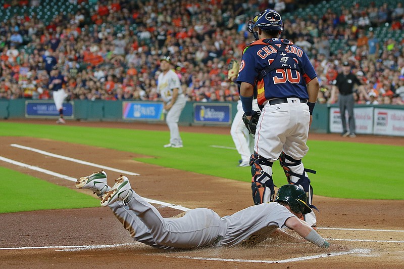 Oakland Athletics' Boog Powell dives safely into home plate as he scores on a throwing error as Houston Astros catcher Juan Centeno stands by in the first inning of a baseball game, Sunday, Aug. 20, 2017, in Houston. 
