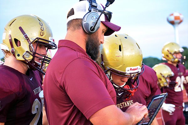 Eldon assistant coach Chad Hult reviews a play on a tablet with Eldon players on the sideline during last Friday's game against Owensville in Eldon.