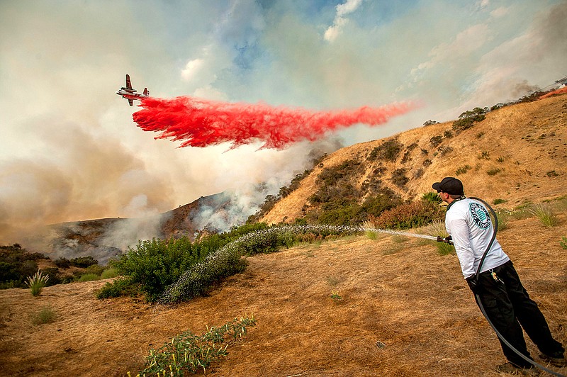 Aaron Funk waters down the hillside behind his parents' home as a plane makes a drop in Sun Valley neighborhood, north of Los Angeles on Saturday, Sept. 2, 2017. The wildfire just north of downtown had grown to the largest in city history, Mayor Eric Garcetti said. 