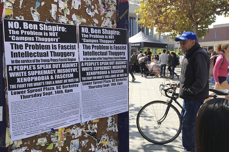 In this Sept. 8, 2017, photo, a man stands by flyers on a University of California, Berkeley campus bulletin board calling for a protest against right-wing speaker Ben Shapiro in Berkeley, Calif. The university will seal off large parts of its campus like a fortress with a closed perimeter and a "very large" visible police presence Thursday, Sept. 14. City and campus authorities anticipate demonstrations at a speech by conservative commentator Ben Shapiro, a former Breitbart editor, and are preparing for possible violence with a variety of new strategies and tightened security. (AP Photo/Jocelyn Gecker)