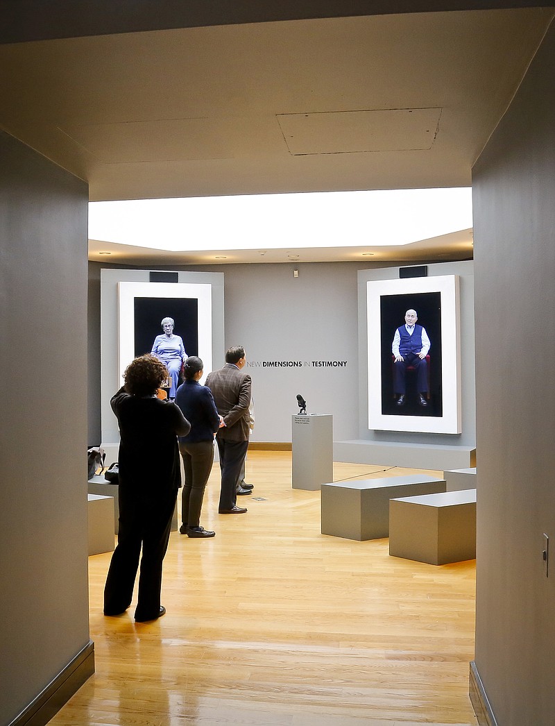 In this Friday Sept. 15, 2017, photo, people view virtual versions of Holocaust survivors Eva Schloss and Pinchas Gutter at the Museum of Jewish Heritage's "New Dimensions in Testimony" exhibit, in New York. Visitors can ask them questions which are answered based on hours of recorded interviews. (AP Photo/Bebeto Matthews)