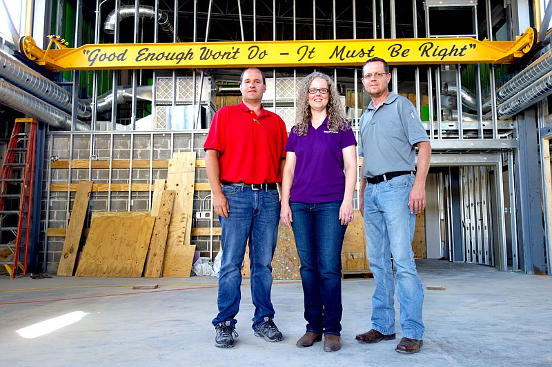 Chief Engineer Gary Nickamp, left, Vice President Janea Danuser and co-Vice President Glenn Danuser, of Danuser Machine Co., stand in the company's new expansion. Behind them, founder Kasper Berry Danuser's slogan hangs on the wall, printed onto an antique crane.