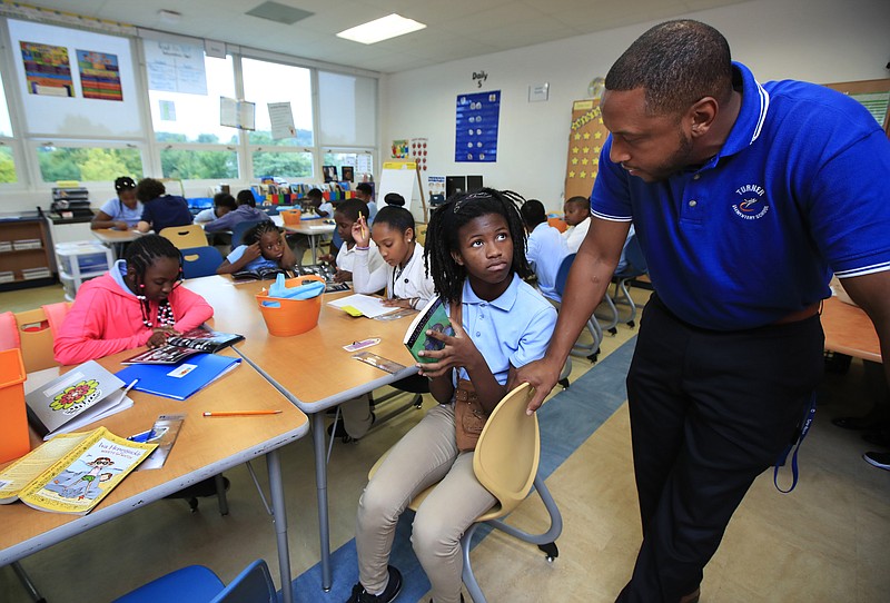 In this Aug. 29, 2017, photo, Turner Elementary School Principal Eric Bethel, right, talks to fifth grade student Kierra Porter, during her reading class, at Turner Elementary School in southeast Washington. Most of the states that first endorsed the Common Core academic standards are still using them in some form, despite continued debate over whether they are improving student performance in reading and math. Bethel says the new guidelines push students to learn “not only the how, but also the why behind the mathematics. Students are learning more and what’s expected of them is much more rigorous than before,” Bethel said.  (AP Photo/Manuel Balce Ceneta)