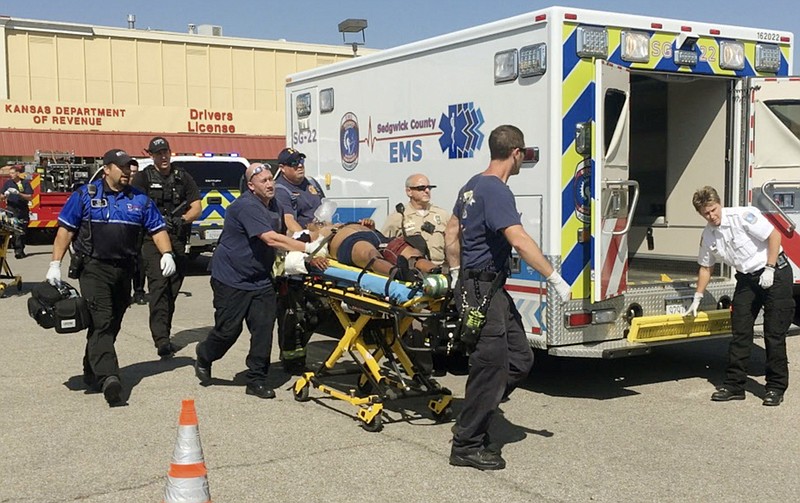 In this Tuesday, Sept. 19, 2017 photo, EMS workers wheel out Kansas Department of Revenue tax seizure agent Cortney Holloway after he was shot at his office in Wichita, Kan. A man suspected in the shooting was under investigation by the agency and owed nearly $200,000 in unpaid sales taxes related to his construction business, according to police and records. Holloway was in stable condition Wednesday. (Fernando Salazar /The Wichita Eagle via AP)
