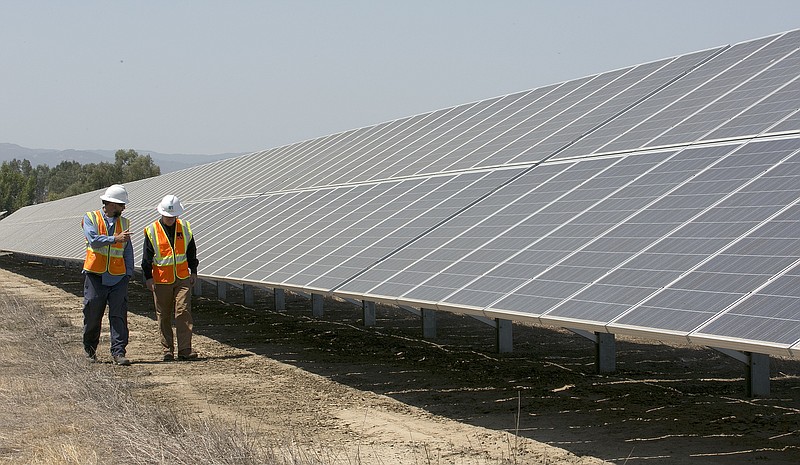 FILE - In this Aug. 17, 2017, file photo, solar tech Joshua Valdez, left, and senior plant managerTim Wisdom walk past solar panels at a Pacific Gas and Electric Solar Plant, in Dixon, Calif. Cheap solar panels imported from China and other countries have led to a boom in the U.S. solar industry, where rooftop and other installations have surged 10-fold since 2011. But two U.S. solar manufacturing companies say the flood of imports has led one to bankruptcy and forced the other to lay off three-quarters of its workforce. (AP Photo/Rich Pedroncelli, File)