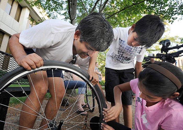 From left, Venkata Garikapaty and his ten-year-old twins, Arjun and Anagha, learn how to fix a flat tire Monday during the bicycle maintenance workshop at the Missouri Regional Library. The workshop was co-hosted by the library and Red Wheel Bike Shop.