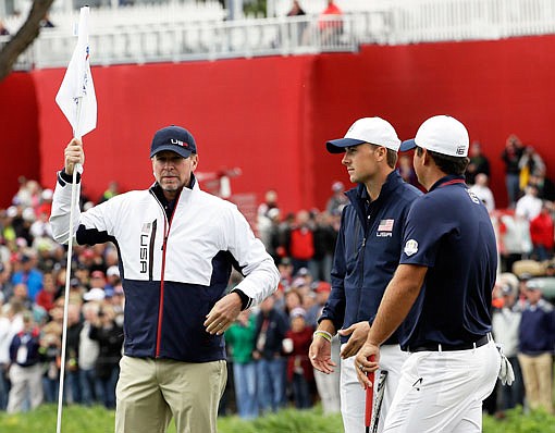 In this Sept. 28, 2016, file photo, United States vice-captain Steve Stricker holds a flag for team members Jordan Spieth and Patrick Reed during a practice round for the Ryder Cup at Hazeltine National Golf Club in Chaska, Minn. Stricker will serve as team captain for the U.S. in this week's Presidents Cup.