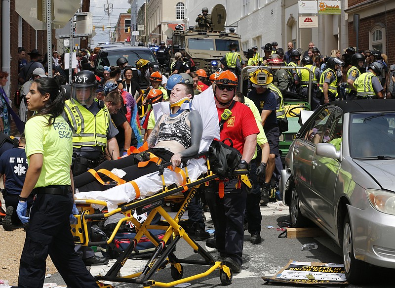 FILE - In this Aug. 12, 2017 file photo, rescue personnel help injured people who were hit when a car ran into a large group of protesters after a white nationalist rally in Charlottesville, Va. Attacks this summer on counter-protesters in Charlottesville, Virginia, and an empty Air Force recruiting station in Oklahoma had the hallmarks of terrorist attacks. But they weren't prosecuted as such.  (AP Photo/Steve Helber, File)