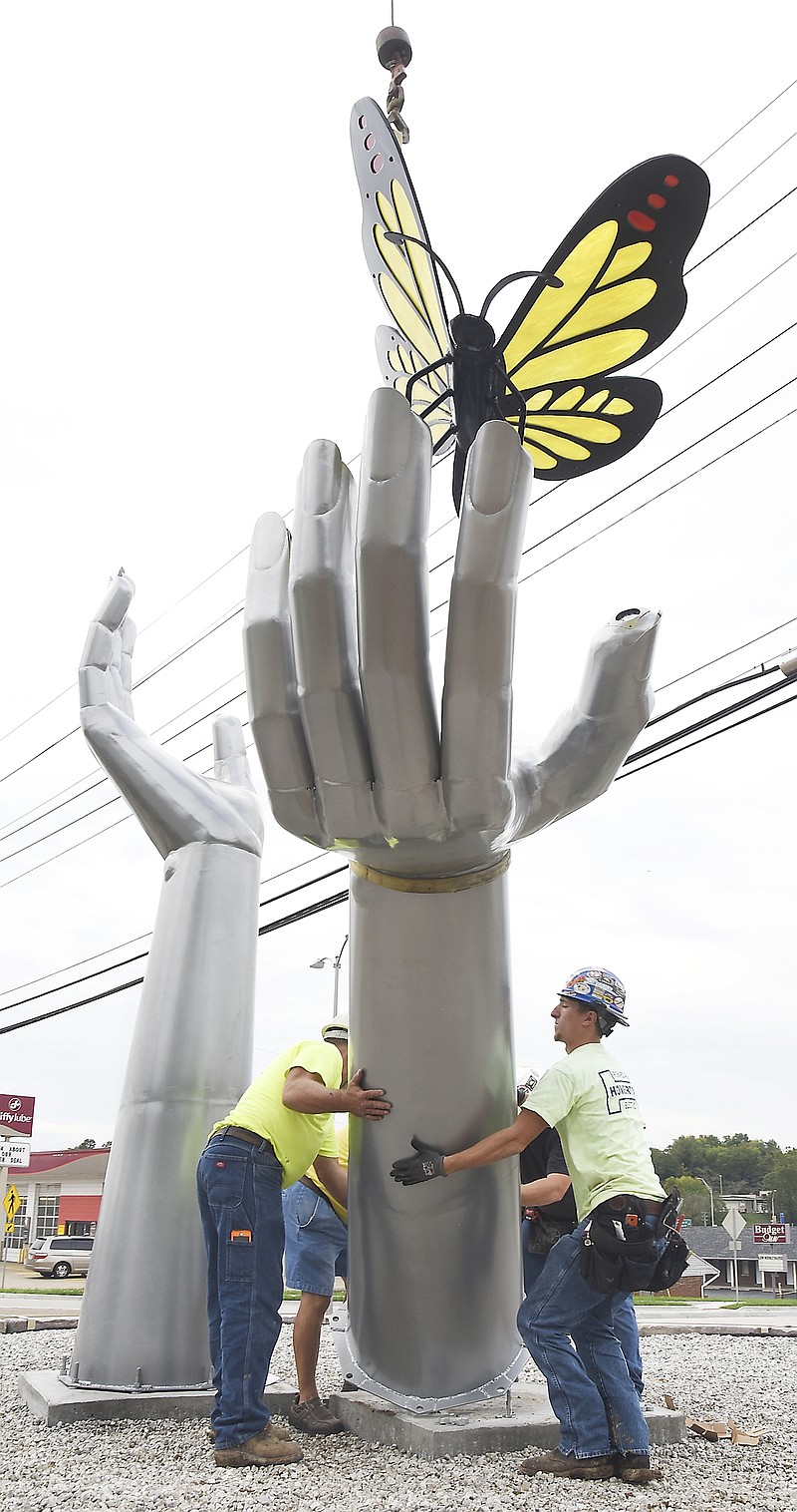 Kyle Schlotz, of Howerton Electric, right, and Don Wolken, of WAVCO, left, work together Friday to install the oversized set of aluminum hands in the middle of the roundabout at Jefferson and Stadium. The sculpture is titled Healing Hands and is the collaborative effort between Mike Mistler and Jim Wisch, created for Capital Region Hospital. The butterfly is made of stained glass set in an aluminum framework, also made by Mistler.