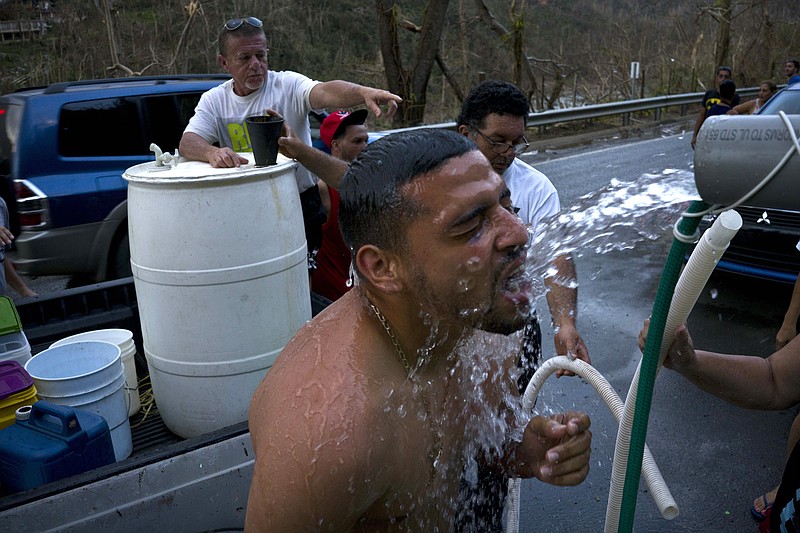 FILE - In this Sept. 28, 2017 file photo, people affected by Hurricane Maria bathe in water piped in from a mountain creek, in Naranjito, Puerto Rico. Four deaths in Hurricane Maria’s aftermath are being investigated as possible cases of a disease spread by animals’ urine, Puerto Rico’s governor said Wednesday, Oct. 11, 2017, amid concerns about islanders’ exposure to contaminated water. On a U.S. territory where a third of customers remain without running water three weeks after the hurricane, some became ill after turning to local streams to relieve their thirst. (AP Photo/Ramon Espinosa, File)