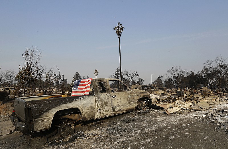 A flag is seen Wednesday, Oct. 11, 2017, draped on the back of a truck destroyed by fires in Santa Rosa, Calif. Wildfires tearing through California's wine country continued to expand Wednesday, destroying hundreds more homes and structures and prompting new evacuation orders.