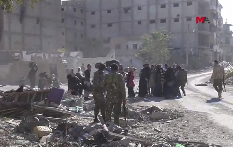This frame grab from a video provided on Friday, Oct. 13, 2017 by Turkey-based Kurdish Mezopotamya agency media outlet that is consistent with independent AP reporting, shows U.S.-backed Syrian Democratic Forces (SDF) fighters, stand around Syrian civilians who fled from the areas that still controlled by the Islamic State militants, in Raqqa, Syria. Scores of civilians including women and children are fleeing the last few remaining neighborhoods held by the Islamic State group in Syria's northern city of Raqqa, ahead of an anticipated final push by U.S.-backed fighters seeking to liberate the city. (Mezopotamya Agency, via AP)