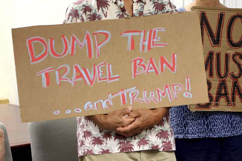 FILE- In this June 30, 2017, file photo, critics of President Donald Trump's travel ban hold signs during a news conference in Honolulu. On Tuesday, Oct. 17, 2017 a federal judge in Hawaii blocked the Trump administration from enforcing its latest travel ban, just hours before it was set to take effect. U.S. District Judge Derrick Watson granted Hawaii's request to temporarily block the policy from taking effect Wednesday. (AP Photo/Caleb Jones, File)