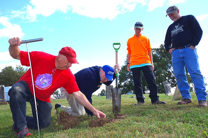 After Michael Barak, second from left, hit a stone with his soil probe, Cliff Martin, Austin Toebben and Ryan Toebben jumped in to help extract a buried grave marker. Barak has discovered over 200 unlabeled graves at Middle River Cemetery in Tebbetts.