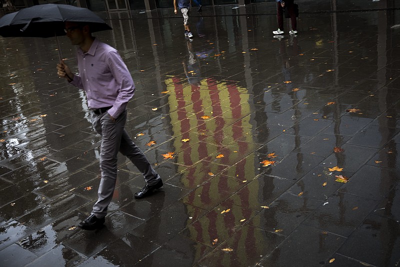 People walk past a Catalan flag reflected on the wet ground in Barcelona, Spain, Thursday, Oct. 19, 2017. Spain's government on Thursday immediately rejected a threat by Catalonia's leader to declare independence unless talks are held, calling a special Cabinet session for the weekend to activate measures to take control of the region's semi-autonomous powers. (AP Photo/Emilio Morenatti)