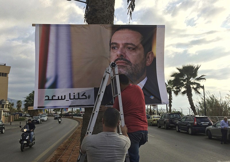 Workers hang a poster of outgoing Prime Minister Saad Hariri with Arabic words that read, "We are all Saad," on a seaside street in Beirut, Lebanon, Thursday, Nov. 9, 2017. Hezbollah has called on Saudi Arabia to stay out of Lebanese affairs, saying the resignation of Prime Minister Saad Hariri, announced from Riyadh over the weekend, "has raised many questions." (AP Photo/Hussein Malla)