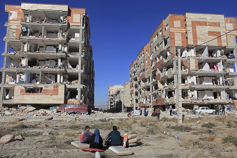 Survivors sit in front of buildings damaged by an earthquake, in Sarpol-e-Zahab, western Iran, Monday, Nov. 13, 2017. A powerful 7.3 magnitude earthquake that struck the Iraq-Iran border region killed more than three hundred people in both countries, sent people fleeing their homes into the night and was felt as far west as the Mediterranean coast, authorities reported on Monday. (AP Photo/Omid Salehi)